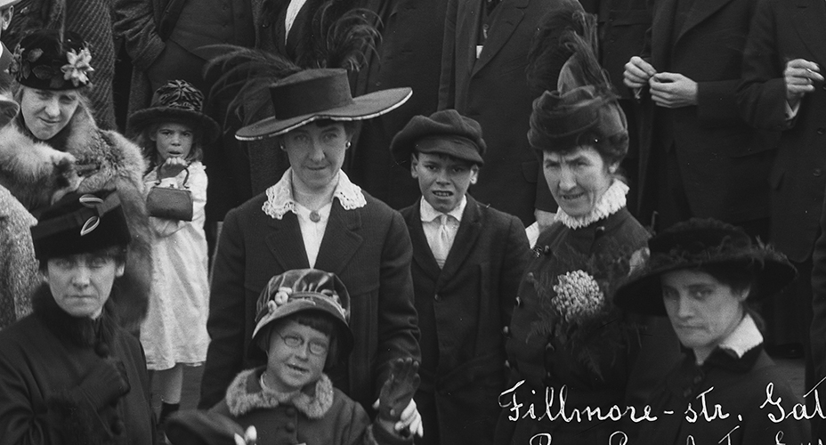 Woman in large hat with children, and a small girl with purse behind her.