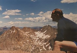 A man seated and staring out over many mountains in the distance