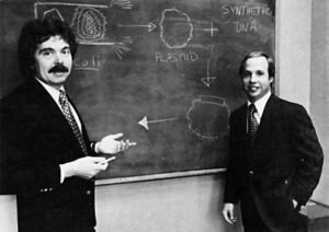 Herbert Boyer and Robert Swanson in front of a blackboard with drawing of recombinant DNA process