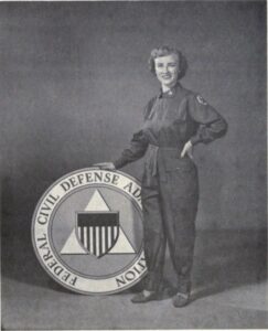 Jean Fuller in coveralls leaning on a sign that says Civil Defense Administration