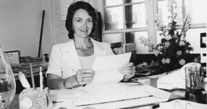 Luella Lilly at her desk, holding up a piece of paper