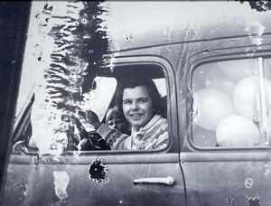 Black and white image of Doris Sloan driving a station wagon full of balloons.