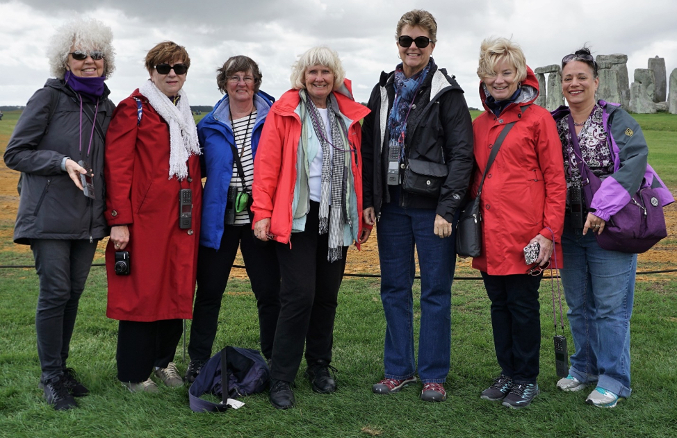 Seven women in jackets standing in front of Stonehenge