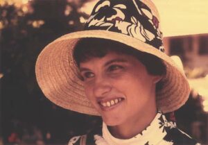 Color photograph of Carolyn Merchant outside and wearing a straw hat with a floral design