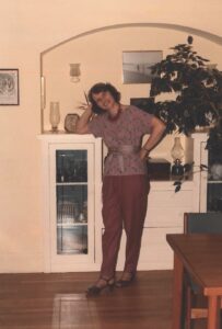 Color photograph of Carolyn Merchant inside a room, leaning on a white cabinet and standing on a dark wood floor