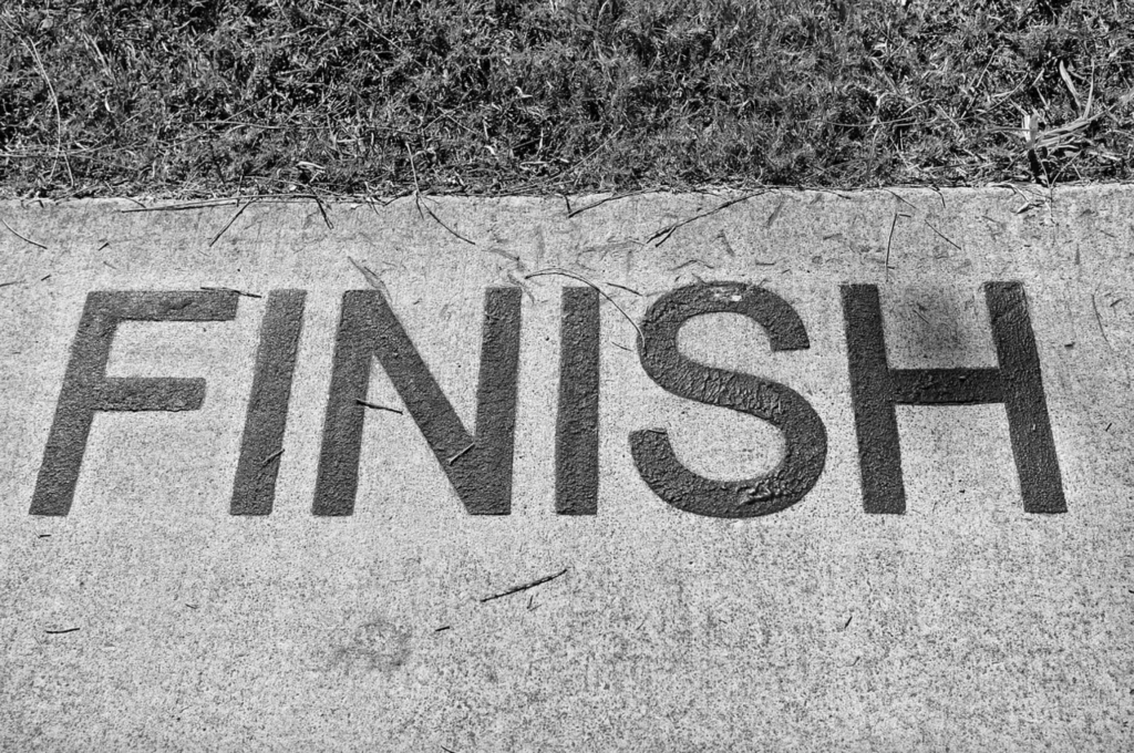 Black and white photograph with grass and concrete with the word "finish" painted on the concrete in large capitalized letters.