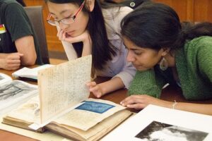 Two students closely studying an old book with yellowed pages