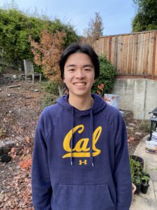 Zachary Matsumoto wears a blue Cal sweatshirt and stands in a yard, smiling at the camera