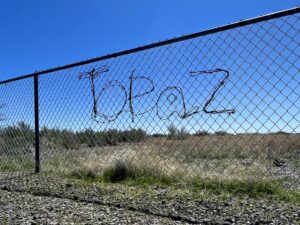 A chain-link fence with the word Topaz shaped out of barbed wire on it