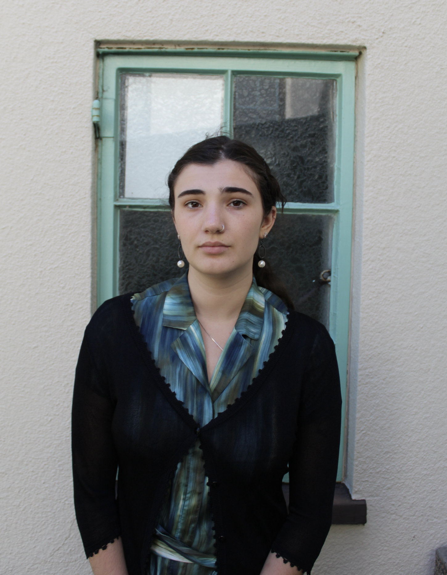 Image of the author, a young woman wearing a blue shirt and black sweater, standing in front of a window.