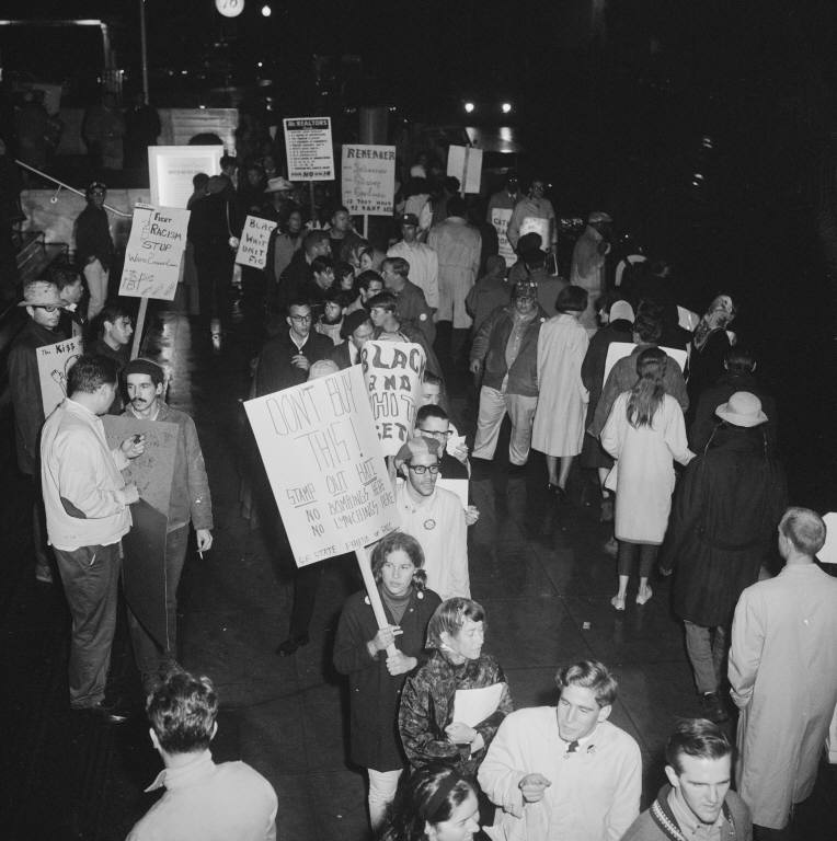 A group of college-aged people stand in a line holding signs. The photo is black-and-white. 