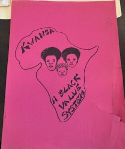 Hot pink flyer for Kwanza celebration, with what looks like a mother, father, and child drawn inside a map of the continent of Africa