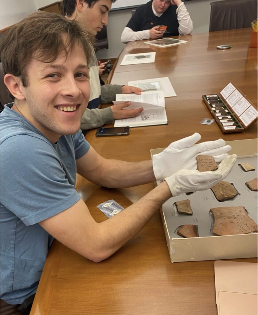 (Ian McLendon holds O.Tebt. 4, a receipt of beer. Behind him, Nicolas Iosifidis and Wilder Burke research and photograph papyri.)